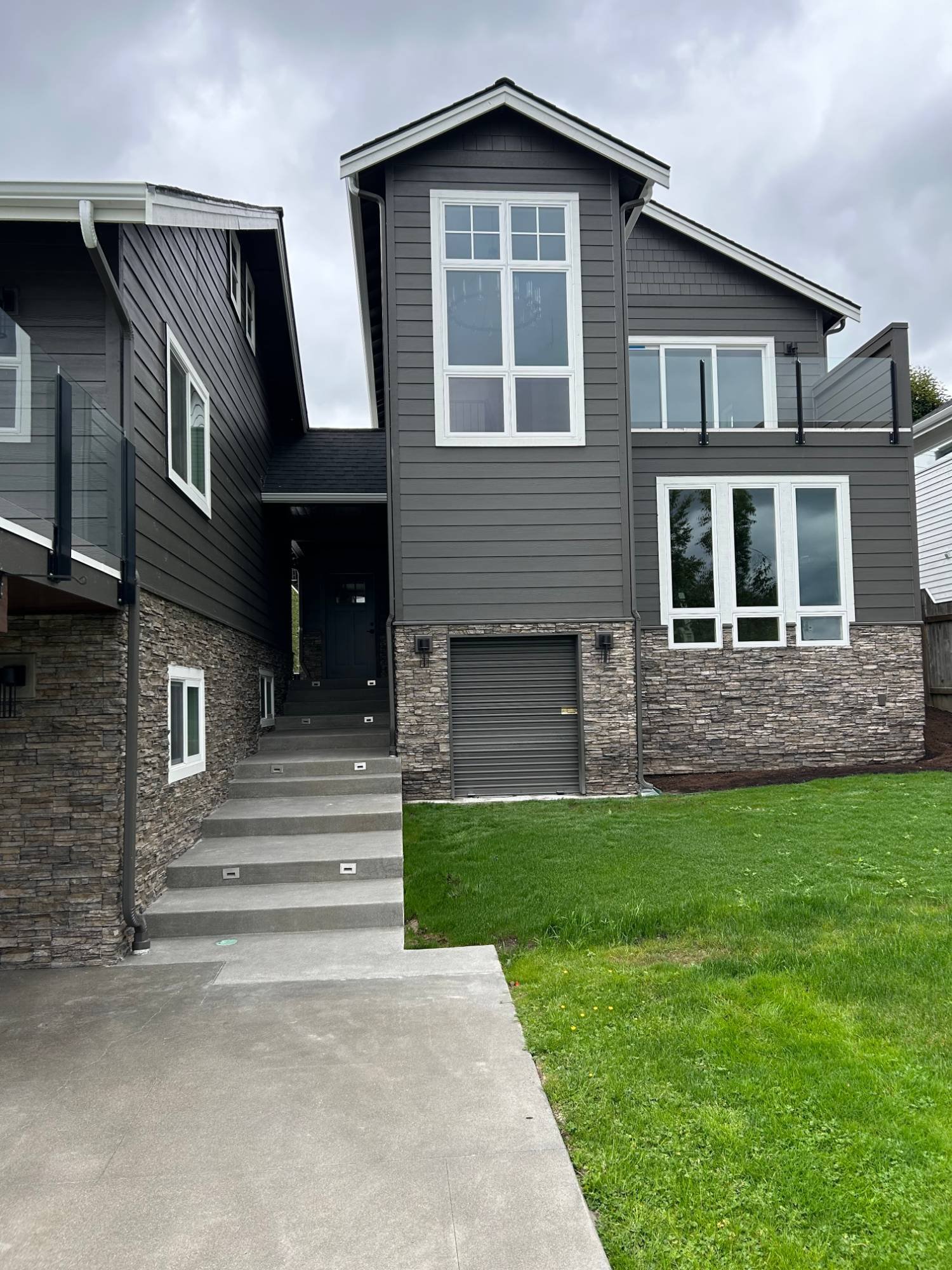 Finished ADU exterior with a tall gable window, stone veneer base and lit concrete steps
