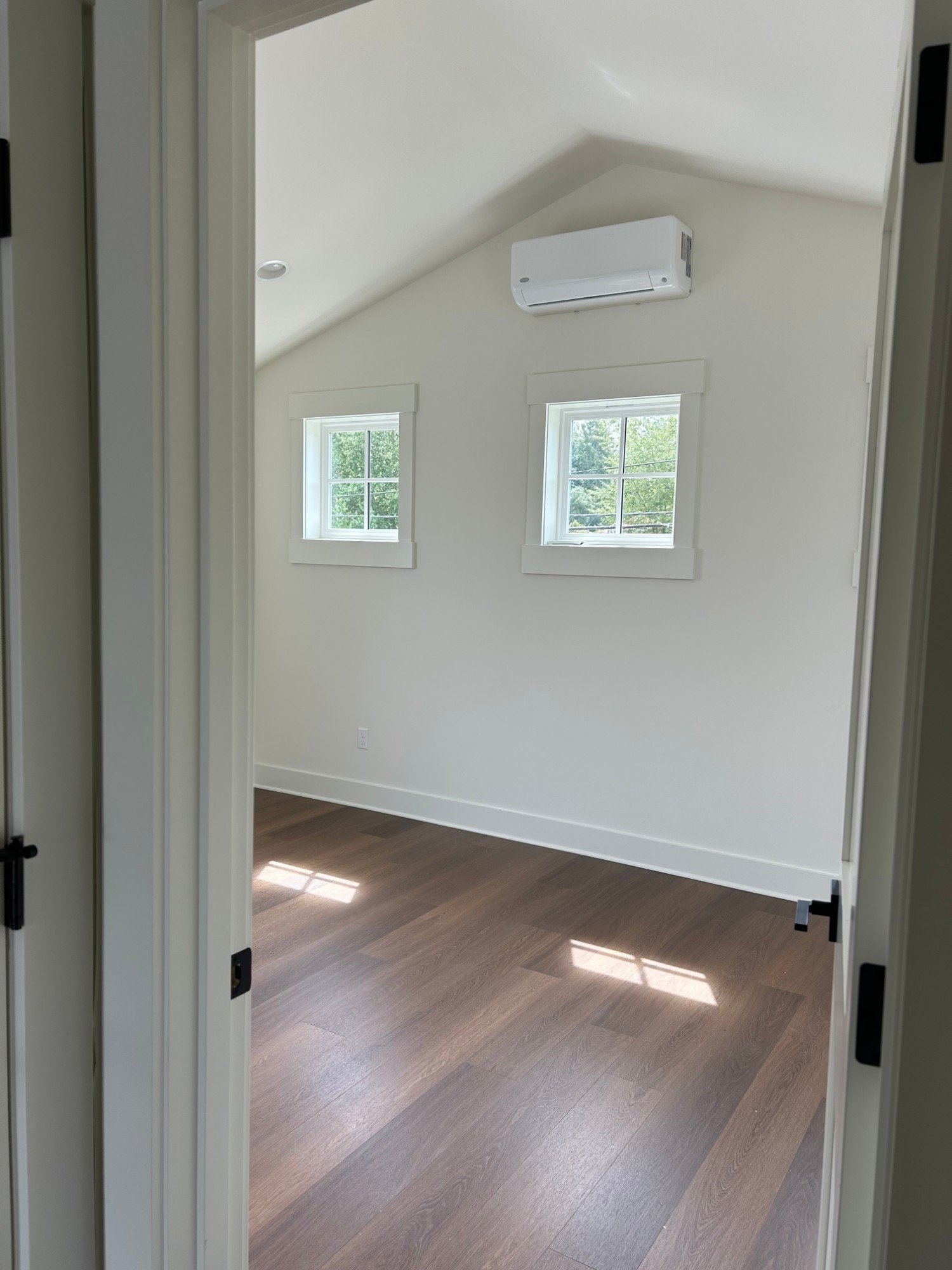 Bedroom with a vaulted ceiling, two small windows and a ductless mini-split