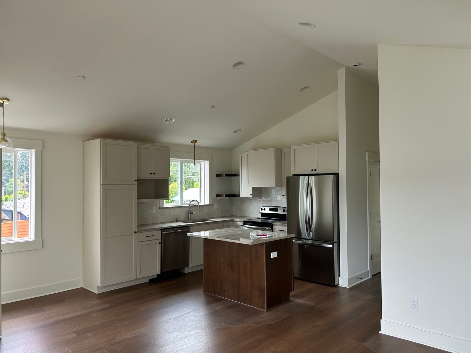 After: ADU kitchen with white shaker cabinets, a wood island, tile backsplash and stainless appliances under a vaulted ceiling