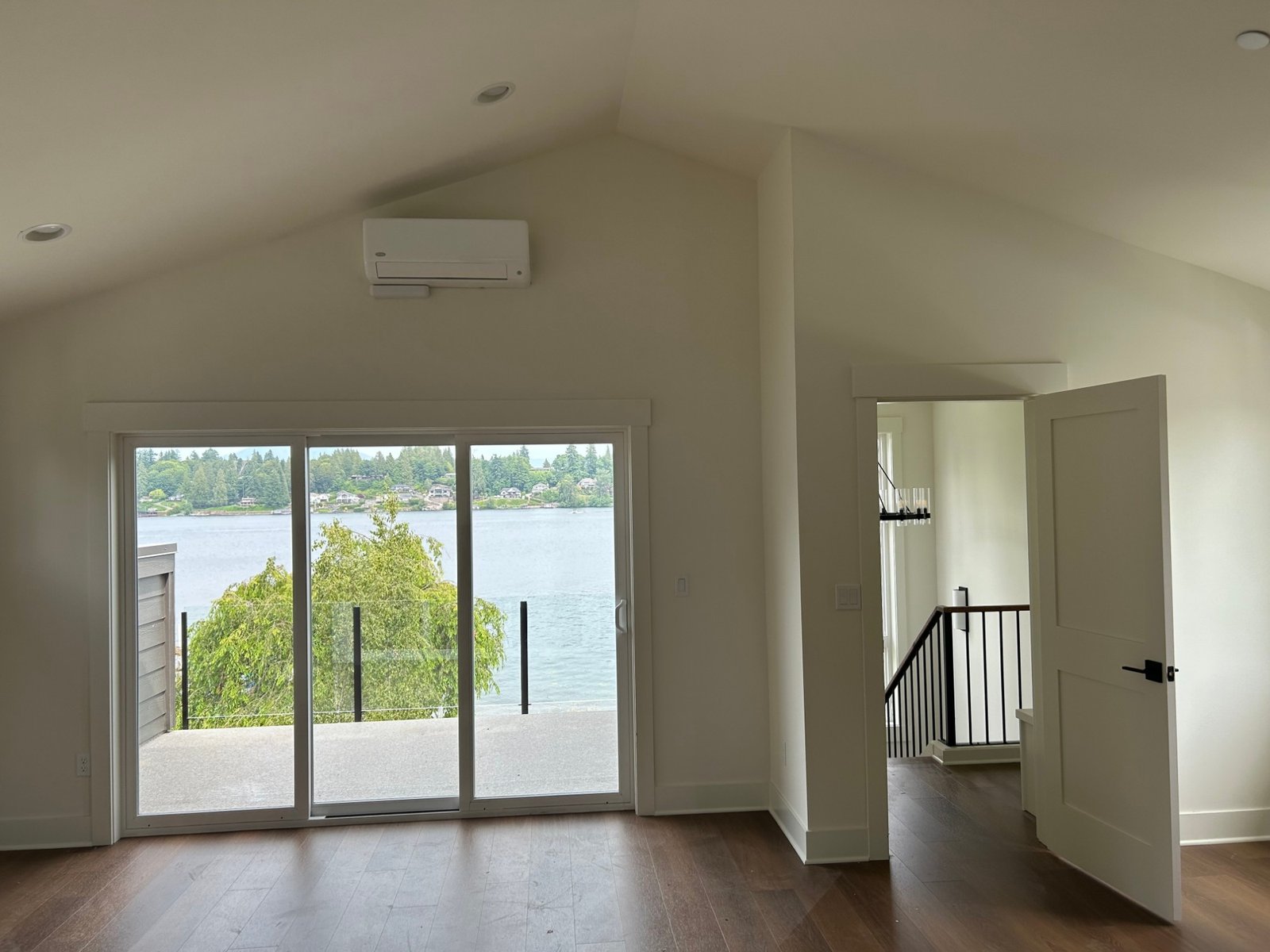 After: vaulted upstairs room with sliding doors opening onto a glass-rail balcony over the lake