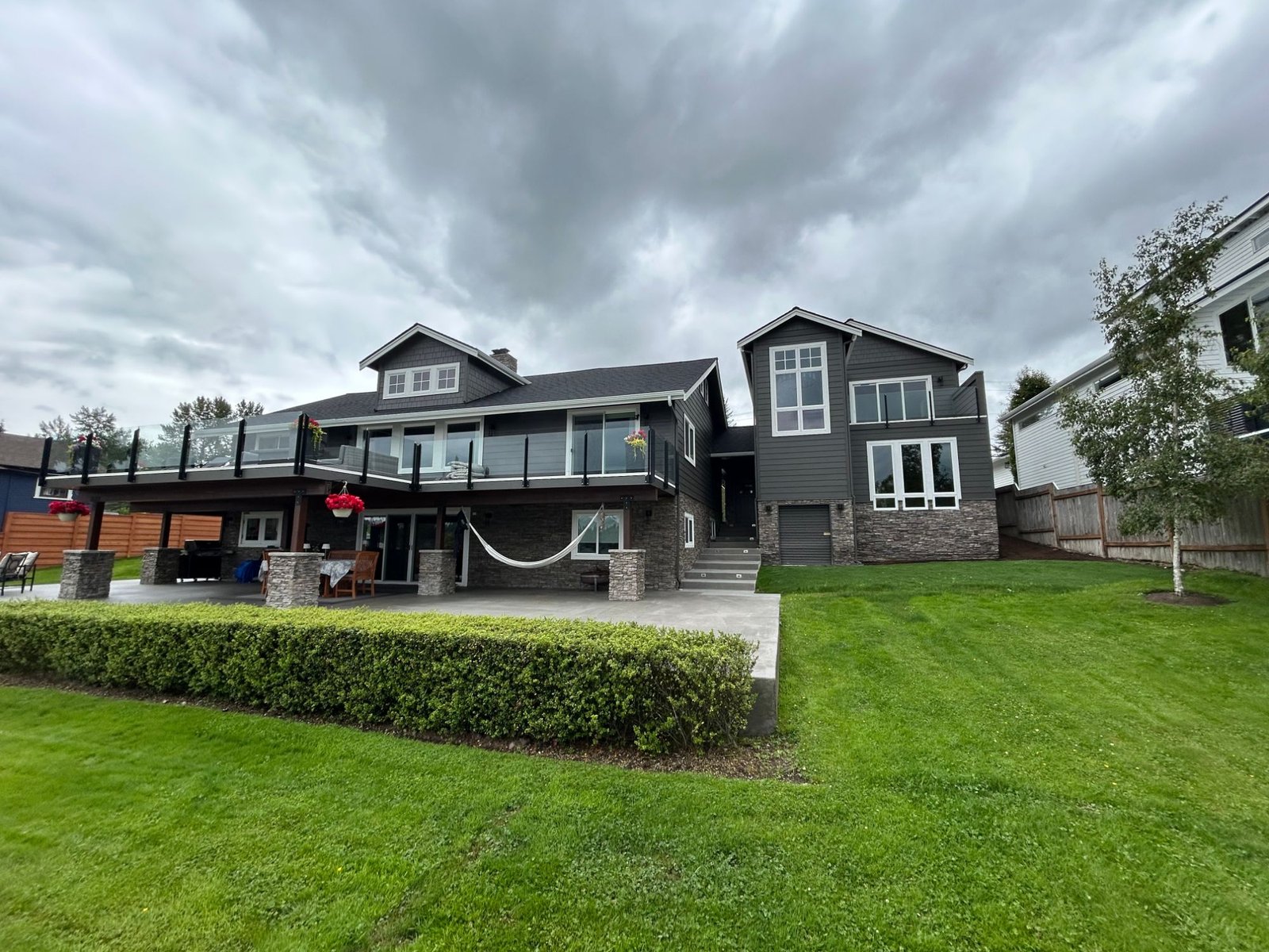 Lake side of the property: the new two-story ADU attached to the main house, both in dark grey siding with stone veneer