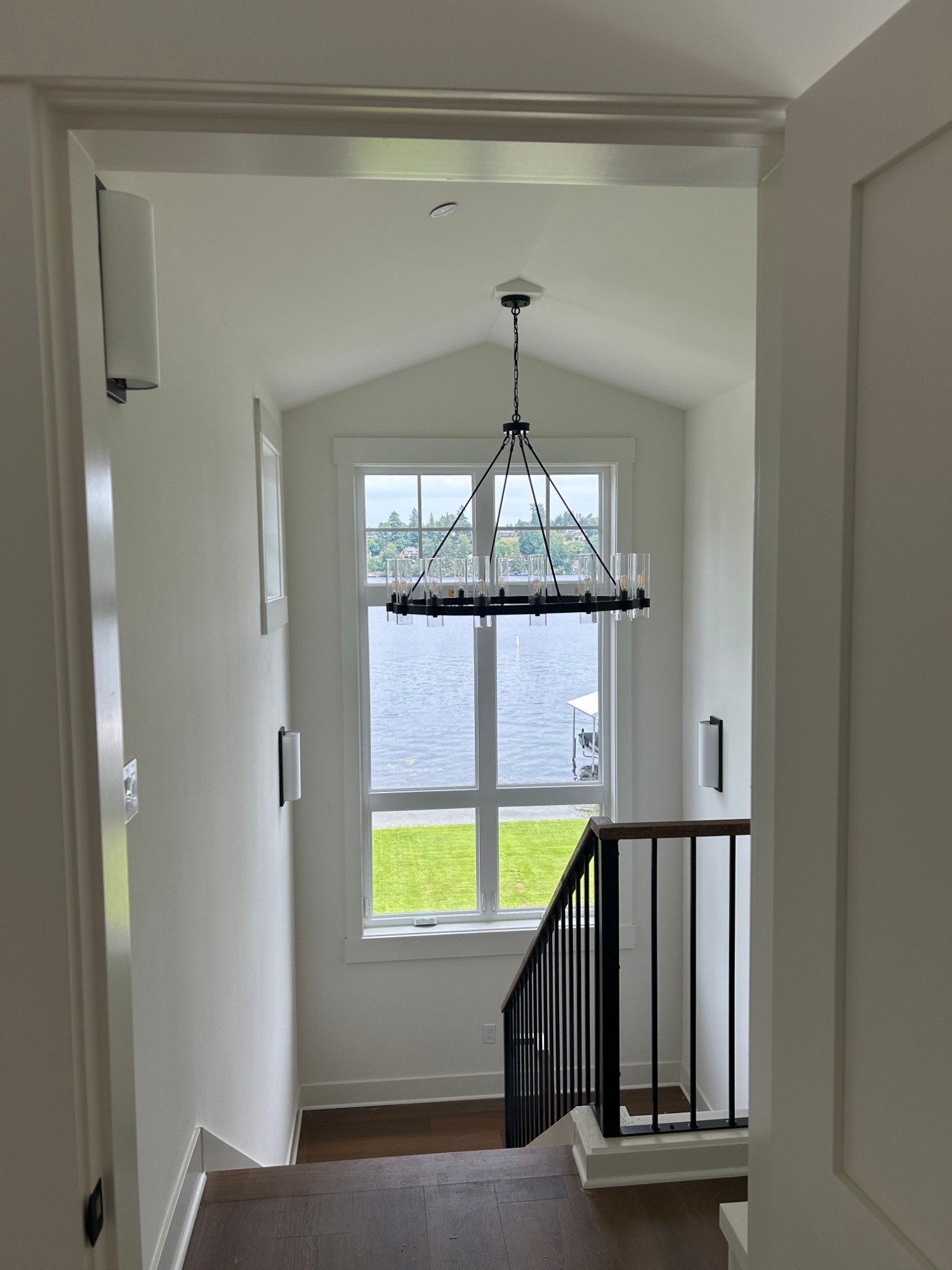 Vaulted stairwell with a ring chandelier in front of a tall window looking out at the lake