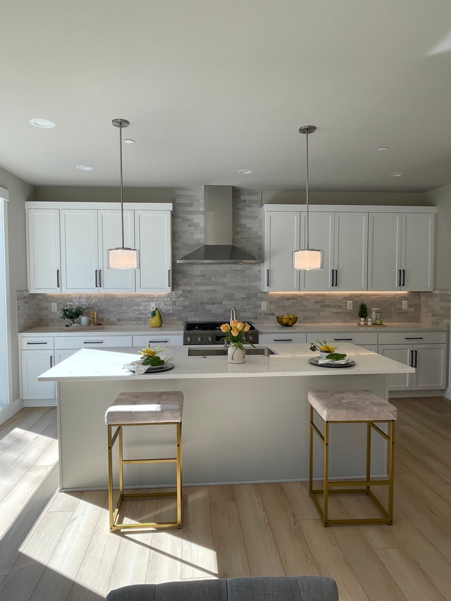 White shaker kitchen with a quartz island, drum pendants and gold-frame stools