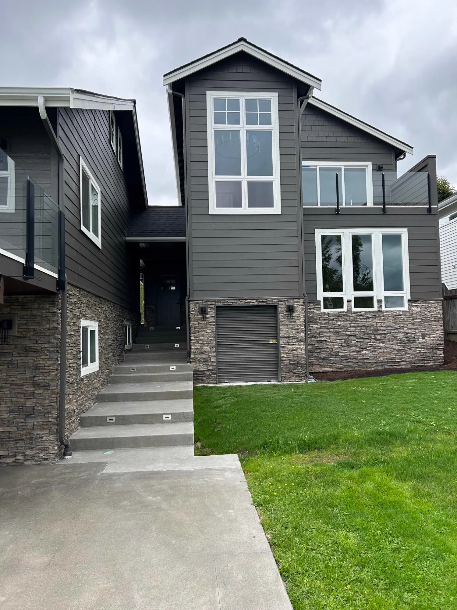 Finished ADU exterior with a tall gable window, stone veneer base and lit concrete steps