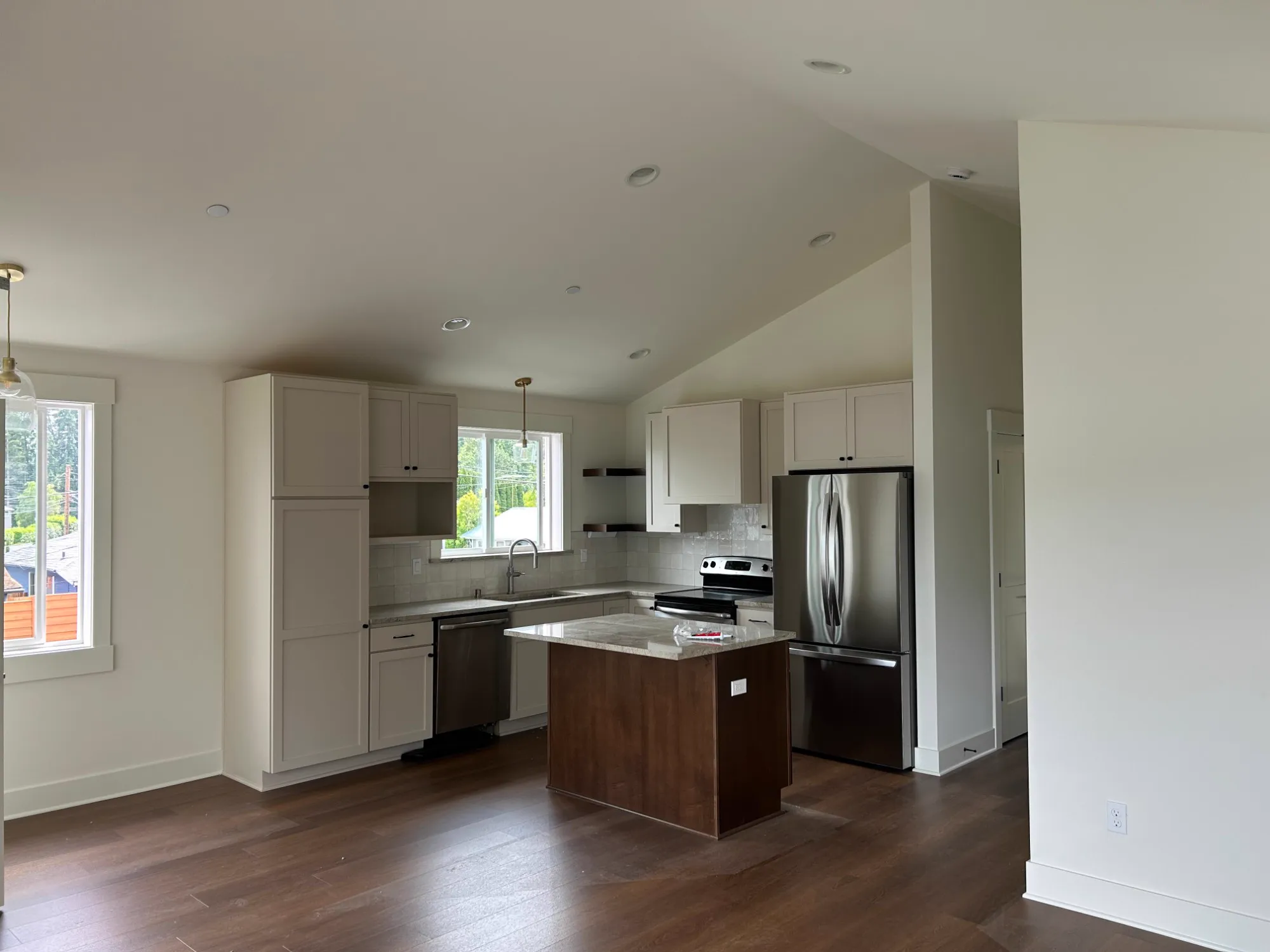After: ADU kitchen with white shaker cabinets, a wood island, tile backsplash and stainless appliances under a vaulted ceiling