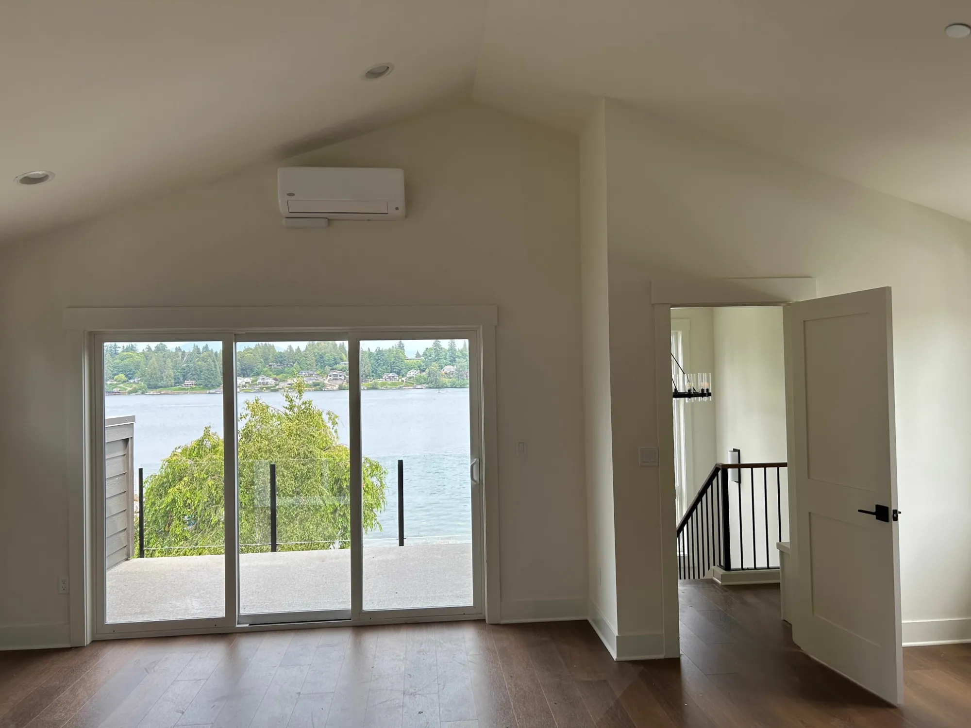 After: vaulted upstairs room with sliding doors opening onto a glass-rail balcony over the lake