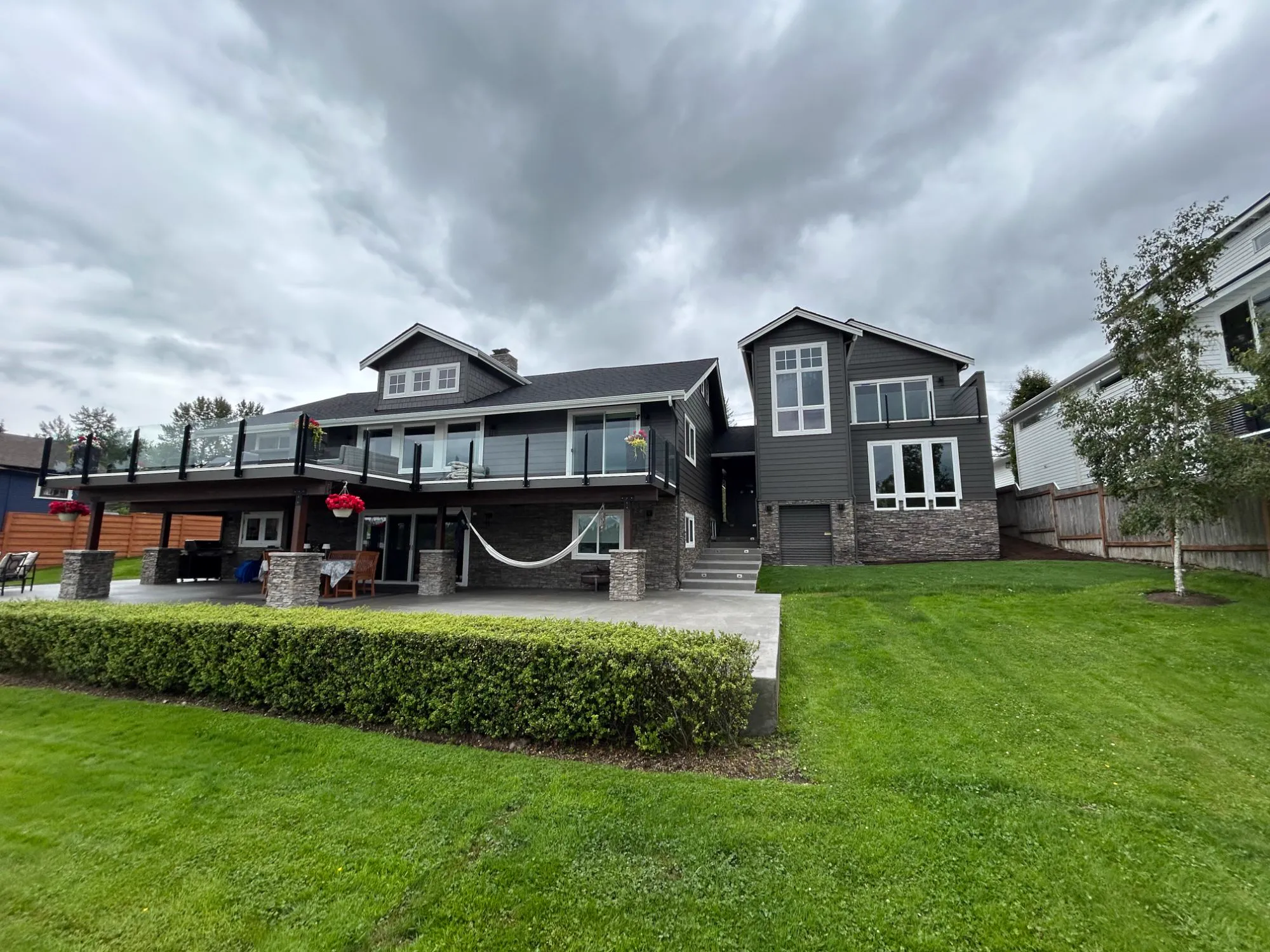 Lake side of the property: the new two-story ADU attached to the main house, both in dark grey siding with stone veneer