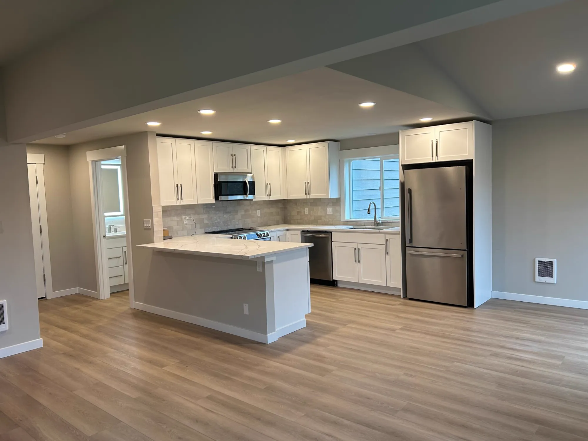 After: white shaker kitchen with quartz peninsula and stainless appliances
