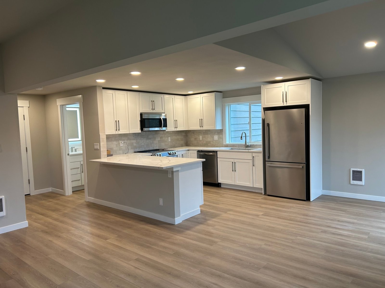 Finished kitchen with white shaker cabinets, quartz peninsula and stainless appliances